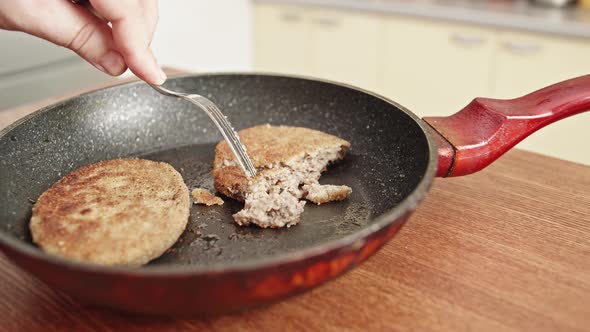 Fish cutlets in a frying pan with oil. Male hand with a fork. alt