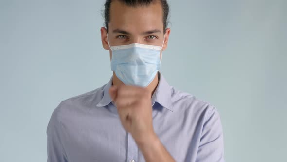 Young man wearing a protective medical face mask coughing from a viral infection. alt