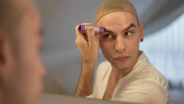 Reflection of LGBT Woman Modelling Eyebrows with Balm Stick Sitting Indoors at Home alt