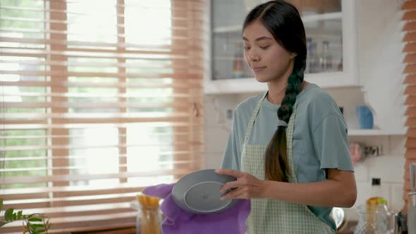 Young asian woman wiping dishware with a cotton towel in the kitchen at home.