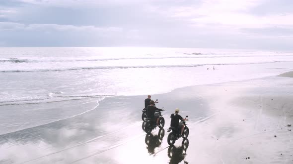 Three Handsome Hipster Men Riding Modern Custom Motorcycle Cafe Racer on the Black Sand Beach Near alt
