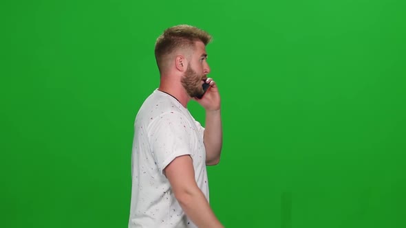 Portrait of Bearded Guy Walking and Talking on Mobile Phone on Green Screen. Chroma Key. Profile alt