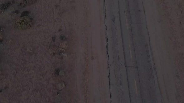 AERIAL: Birds View of Lonely Abandoned Desert Road with Red Car Driving in the Distance  alt