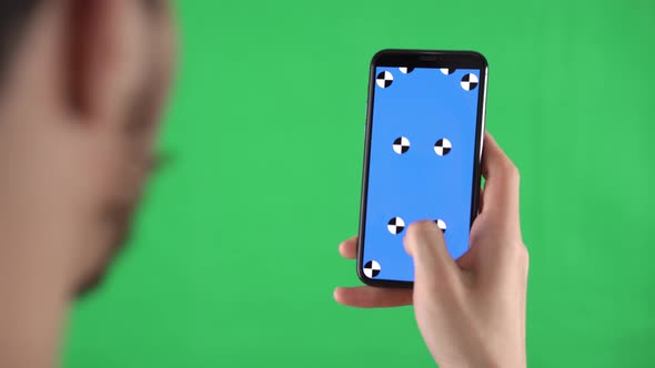 Man is Zooming the Content on the Smartphone with Tracking Markers on Display Against a Green Screen alt