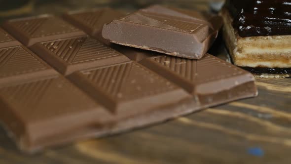 Closeup of a Bar of Chocolate and Broken Pieces Next to a Chocolate Creamy Brownie on a Wooden Table