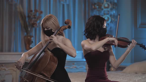 Symphonic duet. Two girls in beautiful dresses and masks play the violin and cello. violin and cello