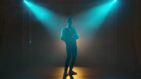 Silhouette a Young Stylish Guy Plays the Golden Shiny Saxophone in the Turquoise Spotlights on Stage alt