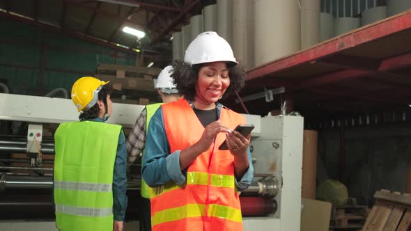 Safety uniform female worker chatting mobile phone and smiling in paper factory. alt