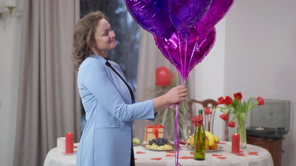Side View Portrait of Happy Excited Adult Woman Releasing Balloons Indoors at Home on Valentine's alt