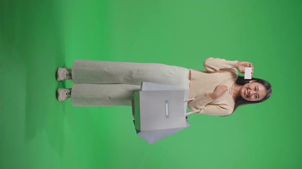 Full View Of An Asian Shopping Woman With Shopping Bags Holding A White Card On Green Screen alt