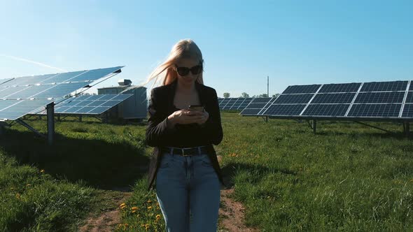 Woman Walks Near Solar Panels Row on the Ground at Sunset and Touch Solar Cells