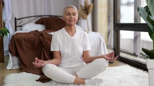 Senior Woman Practicing Yoga in Lotus Positionitting at Domestic Bedroom