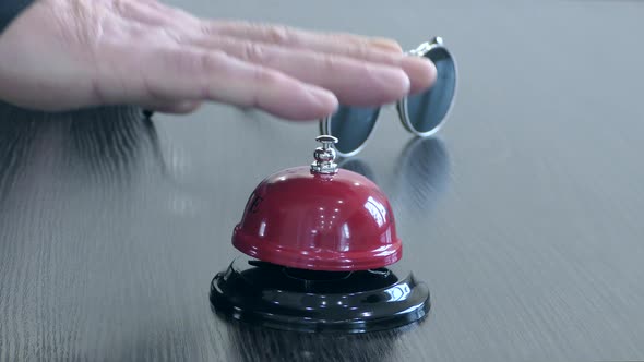 A man's hand rings a bell at the front desk.