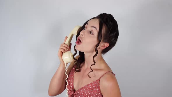 An attractive female model on a white background wearing a vintage dress talking fast on the phone