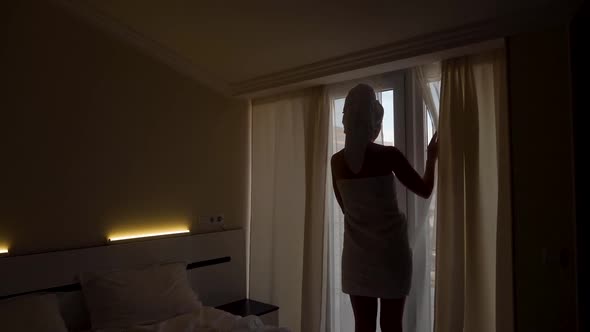 Woman in a Towel After a Bath is Standing Next to an Open Door on the Balcony alt