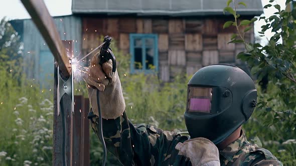 Slow Motion Side View Handyman Welds Carcass of Fence alt