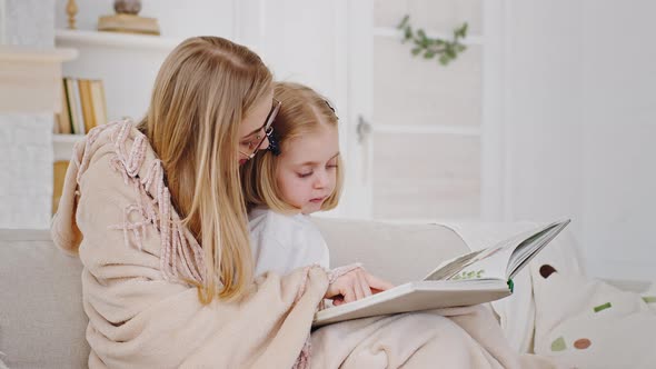 Young Caring Loving Caucasian Mother Wears Glasses Covered Blanket Sitting on Home Sofa with Little alt