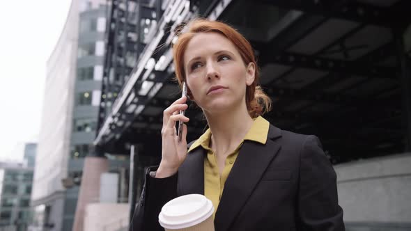 Businesswoman in city using smart phone with takeaway coffee