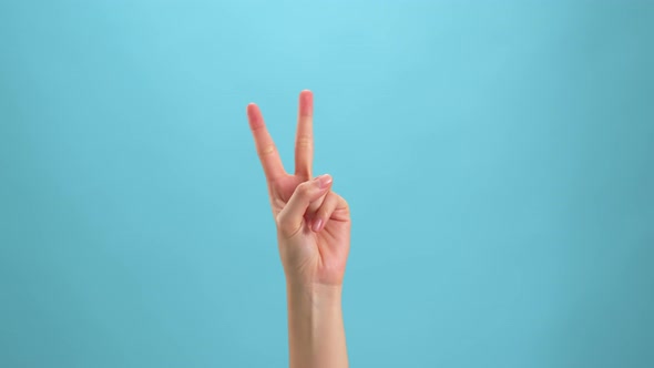 Woman raising two fingers up on hand on the blue background. Concept victory symbol alt