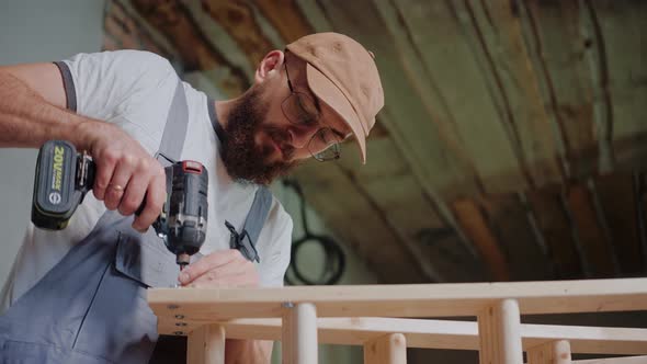 Male Builder Works with Wood Using Electrical Screwdriver in Construction Studio