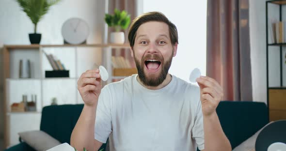 Bearded Guy Sitting in front of Camera and Having Fun while Playing with Cotton pads alt