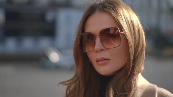 Beautiful Brunette Caucasian Woman in Sunglasses Looking at Camera Standing Outdoors on City Street alt