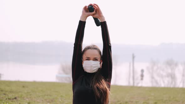 Athletic Woman in a Protective Mask Is Doing Exercise with Dumbbells alt