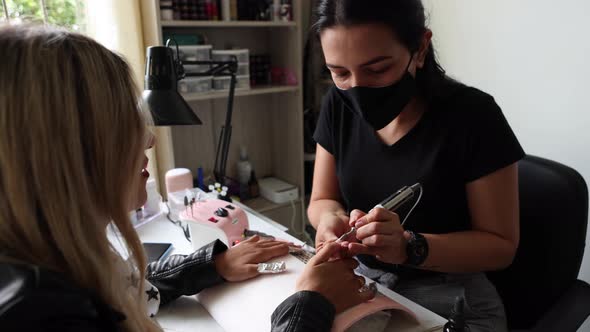 Female master using foil while doing manicure for client in salon alt