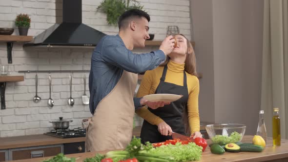 Couple in love preparing vegetarian food in home kitchen, husband feed beloved wife with pizza  alt