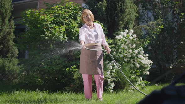 Wide Shot Confident Senior Woman Watering Green Lawn on Backyard in Slow Motion alt
