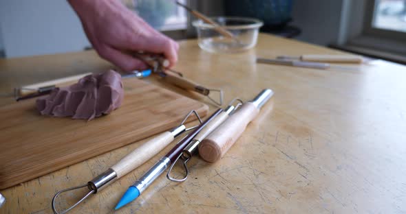 An artist begins to pack up his tools and clean up after sculpting with brown modeling clay in his m alt