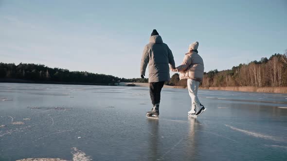 Couple is Skating on a Clear Frozen Lake on a Sunny Day with Beautiful Landscape