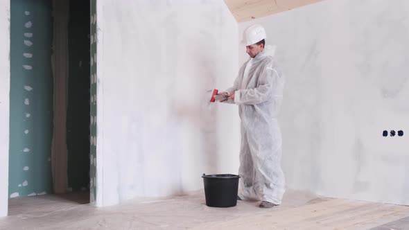 Man with a Spatula in His Hands and a Protective Suit Makes Repairs in the House