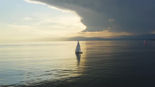 Aerial orbiting around sailboat at sunset on Lake Léman - SwitzerlandDark storm-clouds and rain in alt