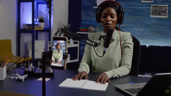 Smiling Influencer African Woman Sitting in Front of Phone Camera Recording alt
