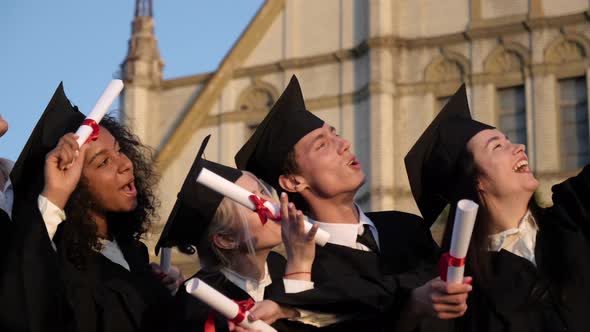 Mixed Races Graduated Friends in Black Traditional Gowns and Caps Making Selfies on the Smartphone. alt