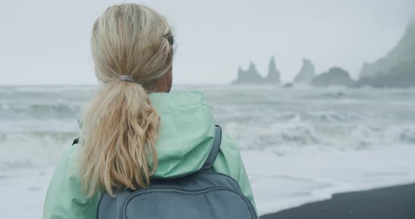 Woman with a Green Raincoat Walking on a Black Sand Beach Enjoying View to Reynisfjara Sea Stack alt