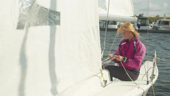 Cute Female Athlete Checks the Ropes Before a Sailing Regatta, Sitting on the Stern of a White Yacht alt