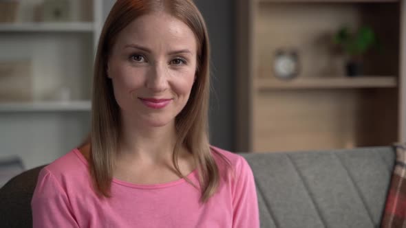 Lovely middle-aged blond woman with a beaming smile sitting on a sofa at home looking at the camera