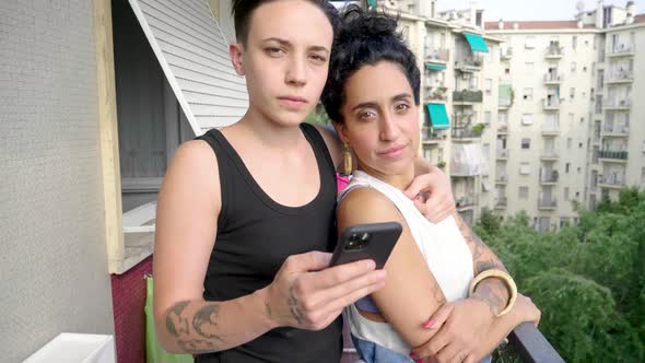 Slow motion shot of lesbian couple using smartphone on balcony alt