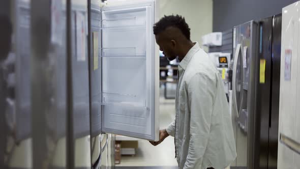 A Man Inspect the Design and Quality of Fridge Before Buying in a Consumer Electronics Store alt
