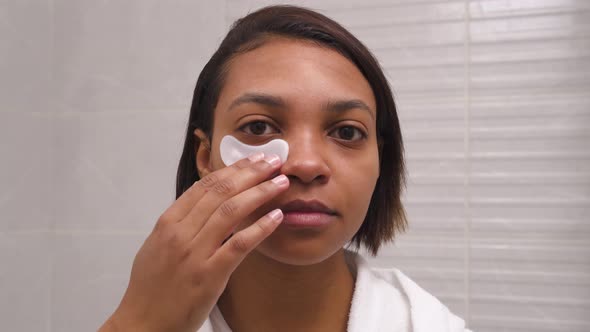 A Woman with Dark Skin Uses Eye Patches Against Wrinkles