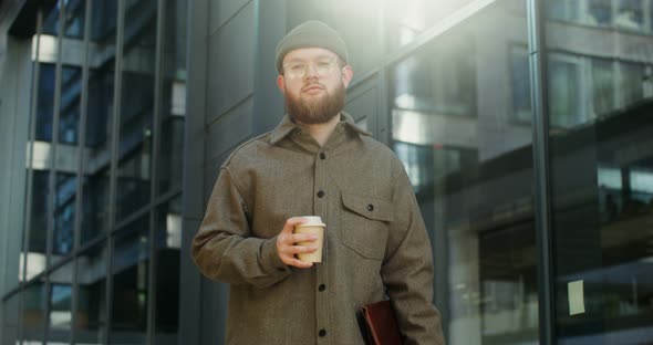 A Bearded Man Standing in the Courtyard of Office Center and Looking at Camera alt