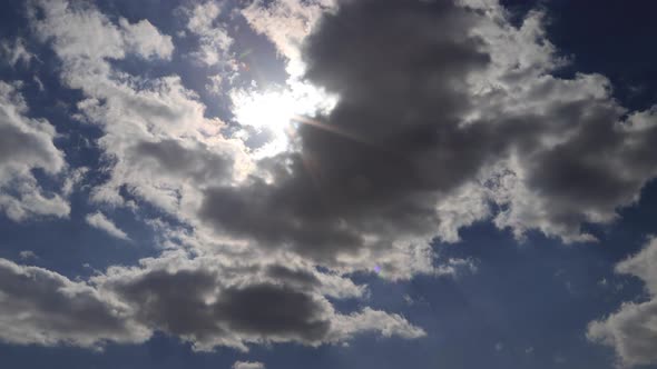Beautiful 4K time lapse. Sun rays break through white fluffy clouds on vivid blue sky