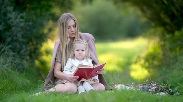 Happy young mum and baby reading a book outdoor beautiful field of sunshine and spring grass
