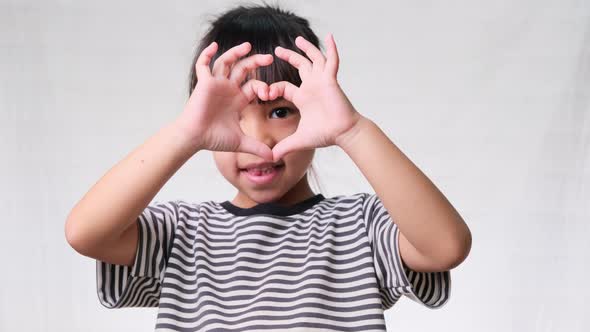 Cute little girl doing heart-shaped hands on eyes over a white studio background. alt