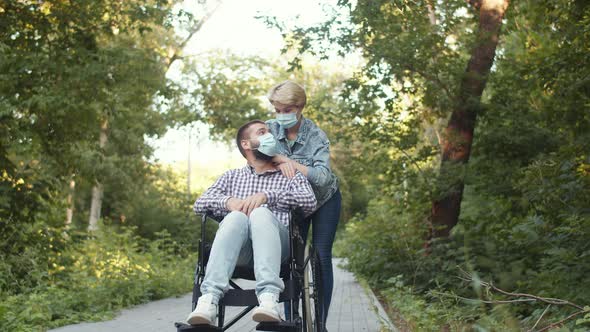Married Couple with Disabled Husband Walk in Masks Along Alleys in Park alt
