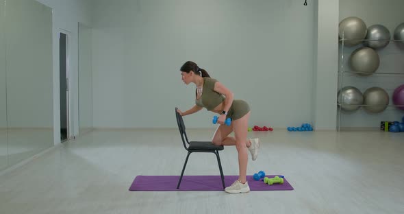 Sports Girl Performs Dumbbell Row to Belt with Emphasis on a Chair