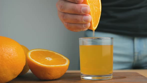 Male hand squeezing out fresh juice from orange citrus fruit into glass in the home kitchen
