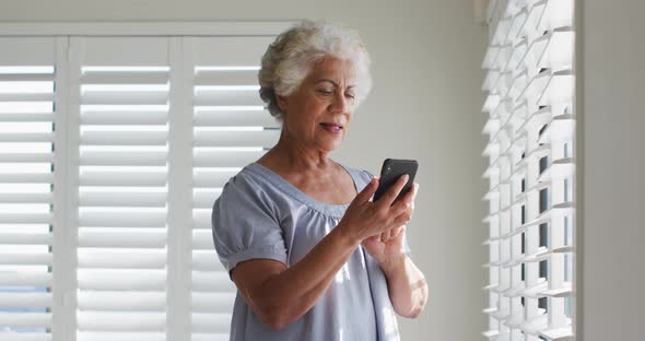 African american senior woman using smartphone and looking out of the window at home alt